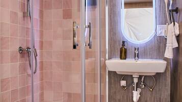 Une salle de bain moderne avec une douche à parois de verre, un plancher en bois et un lavabo surmonté d’un miroir.