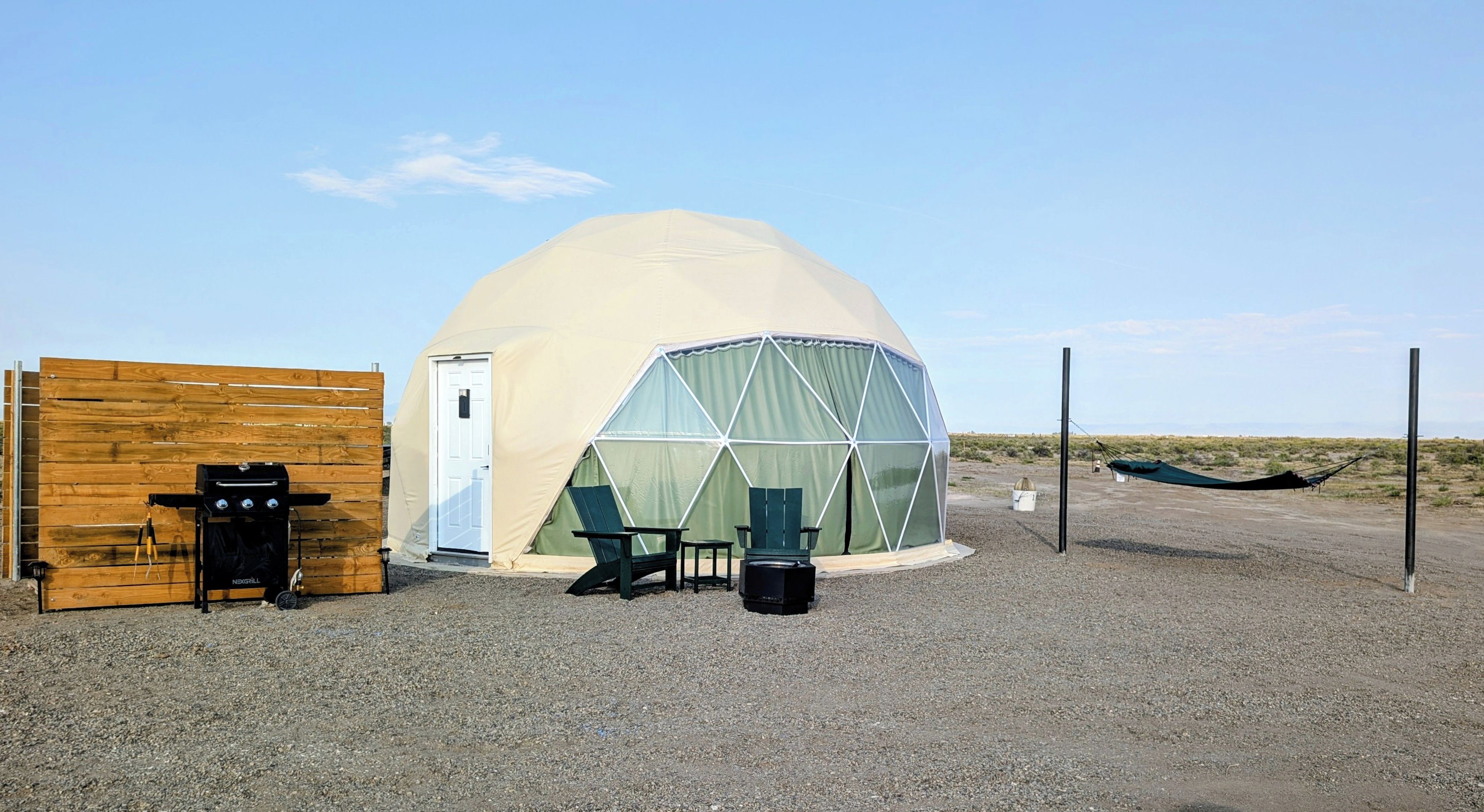 A dome-shaped tent with a door, a grill, two chairs, and a hammock.