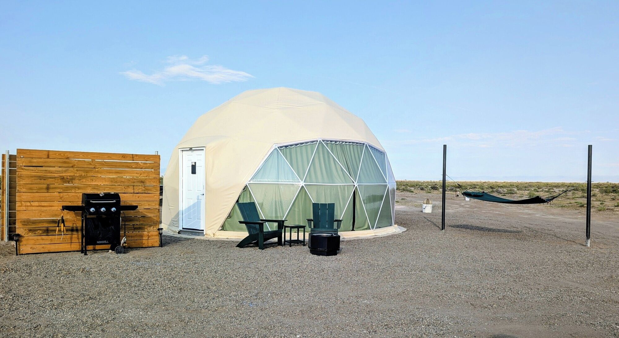 A dome-shaped tent with a door, a grill, two chairs, and a hammock.