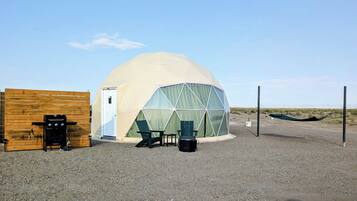 A dome-shaped tent with a door, a grill, two chairs, and a hammock.
