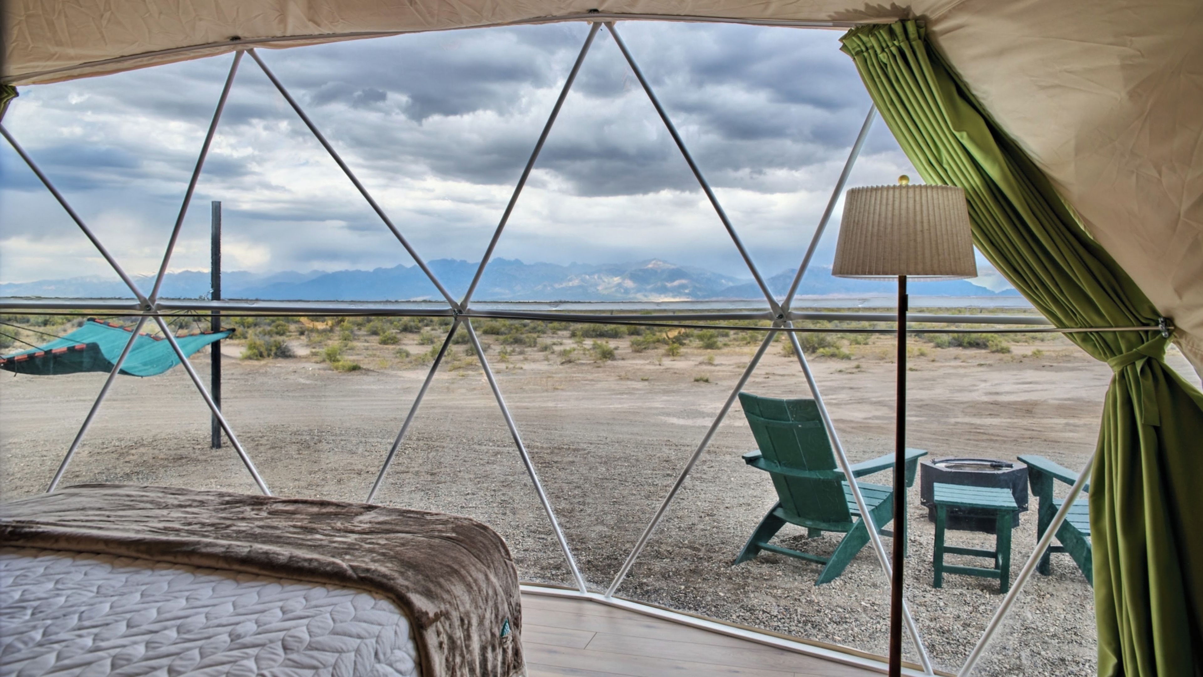 A tent with a bed and chairs, a table, and a view of mountains.