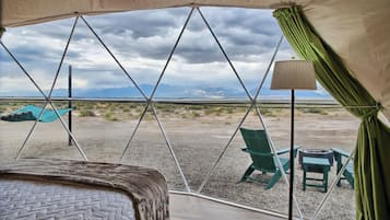 A tent with a bed and chairs, a table, and a view of mountains.