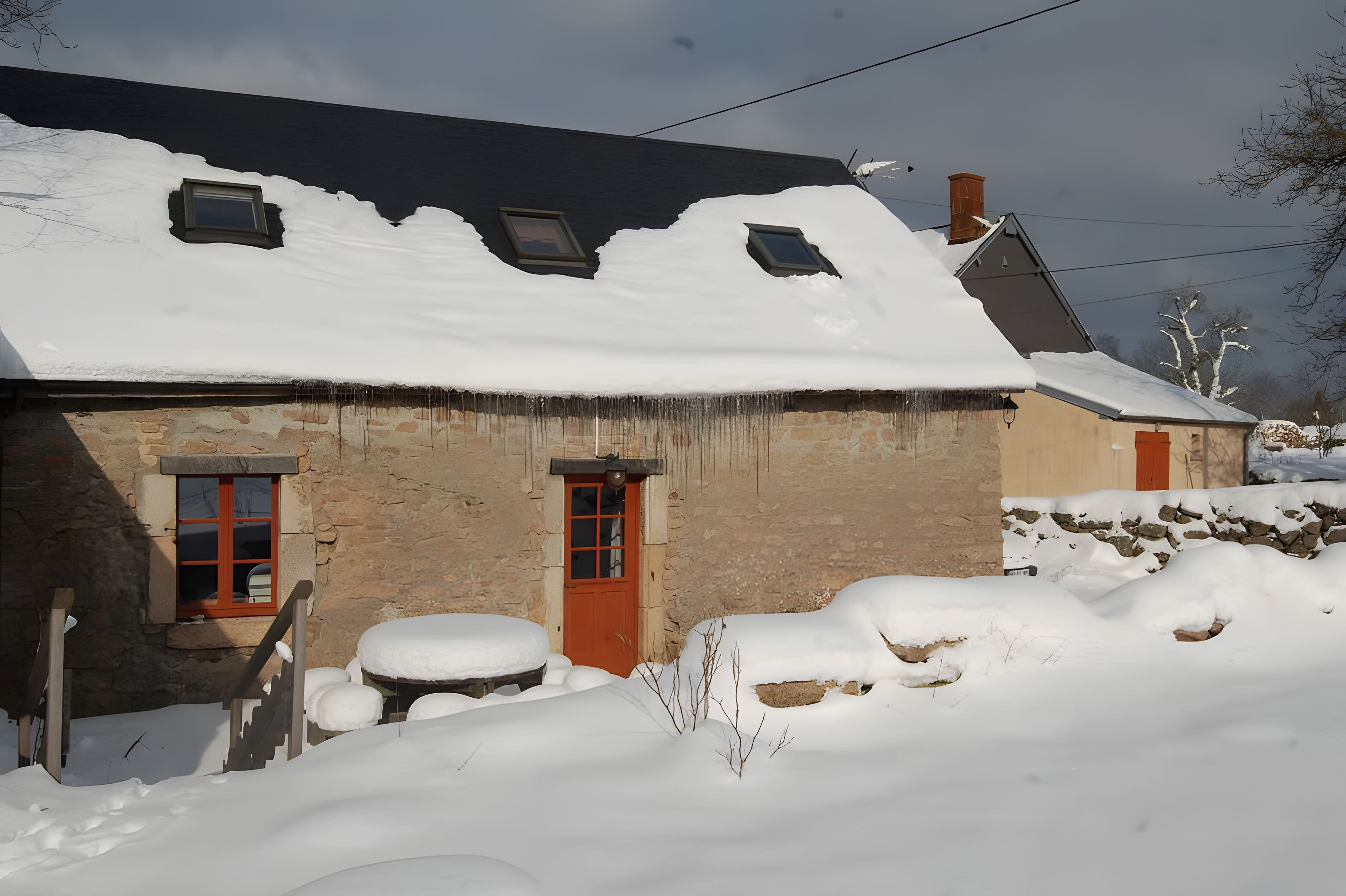 Een stenen huis met een met sneeuw bedekte dak en een rode deur.