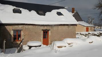 Een stenen huis met een met sneeuw bedekte dak en een rode deur.