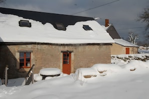 A stone house with a snow-covered roof and a red door. - Morvan Natural Park Gîte with Private Terrace, Garden, and Wi-Fi (Quarré-les-Tombes)