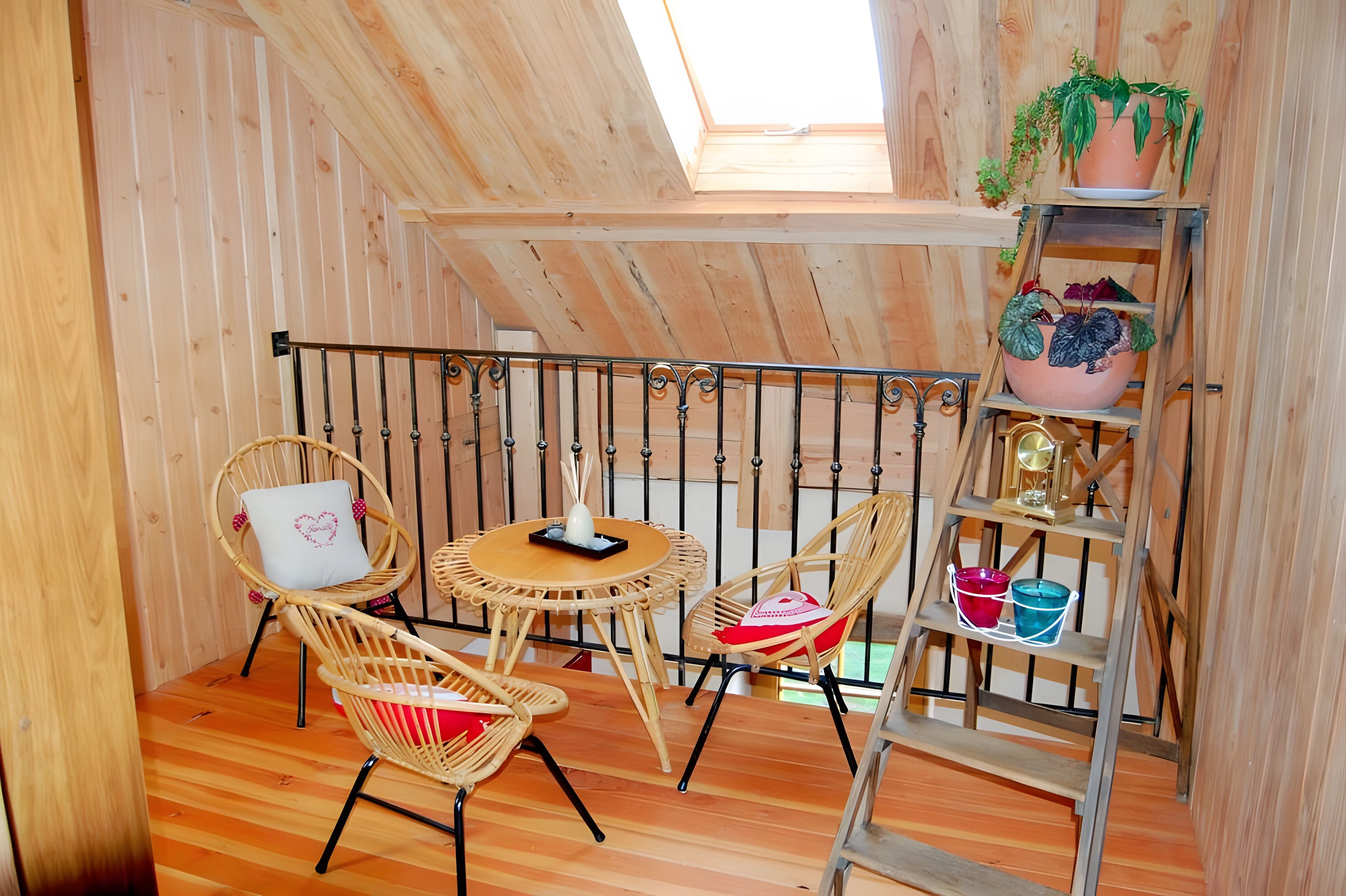Een gezellige houten kamer met een schuine kap, een kleine ronde tafel, rieten stoelen en een houten ladder met plantenpotten.