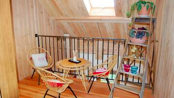 Een gezellige houten kamer met een schuine kap, een kleine ronde tafel, rieten stoelen en een houten ladder met plantenpotten.