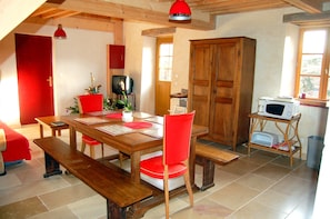 A dining area with a wooden table, red chairs, and a television on a stand. - Morvan Natural Park Gîte with Private Terrace, Garden, and Wi-Fi (Quarré-les-Tombes)