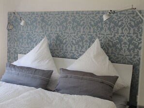 A bed with white and gray striped pillows, a white textured blanket, and a headboard with a patterned wallpaper. - 3 "borkum Flair" (Borkum)
