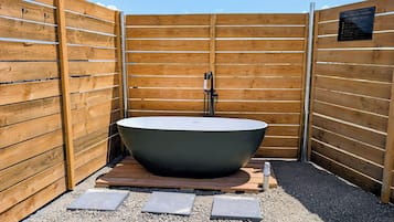 A freestanding outdoor hot tub with a modern design, surrounded by wooden fencing and gravel.
