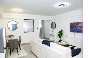 A modern living room with a dining area, a sofa, a TV, and a painting on the wall. - Modern Kilimani Apt with Stunning Nairobi Views! Guest Friendly! (Nairobi)