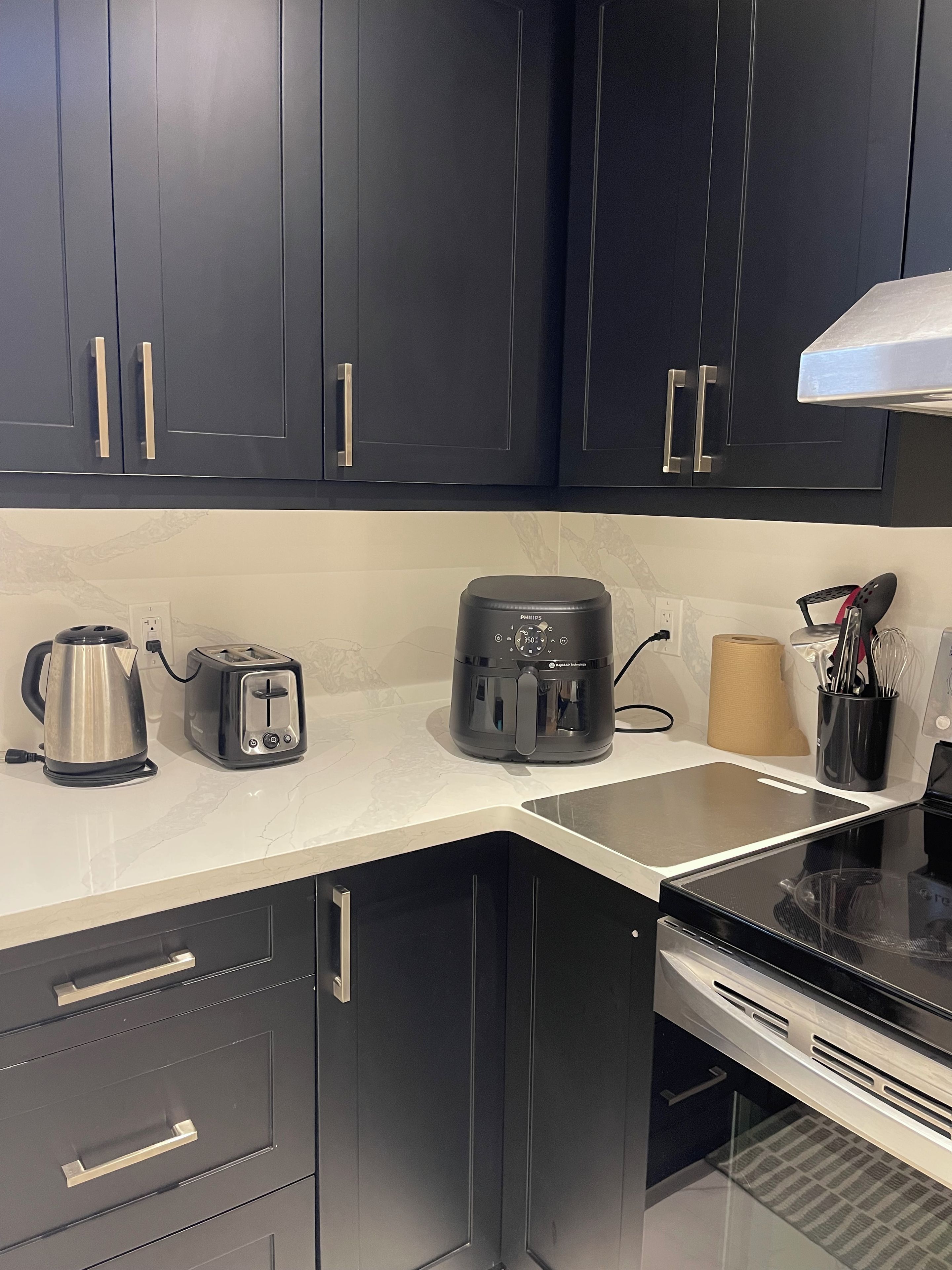 A modern kitchen with dark cabinets, a coffee maker, a kettle, a toaster, and a roll of paper towels.