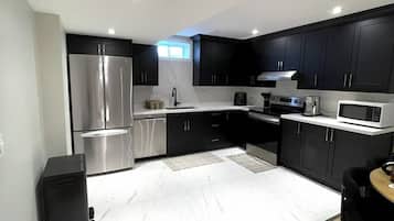 A modern kitchen with dark cabinets, stainless steel appliances, and a white marble countertop.