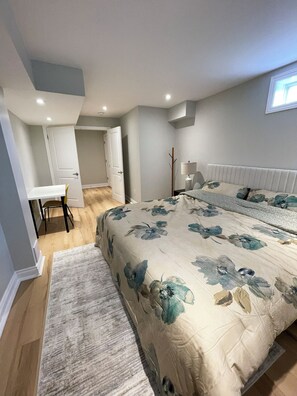 Ein Schlafzimmer mit einem großen Bett, einem Schreibtisch und einem Stuhl. Ein Fenster lässt Tageslicht herein.