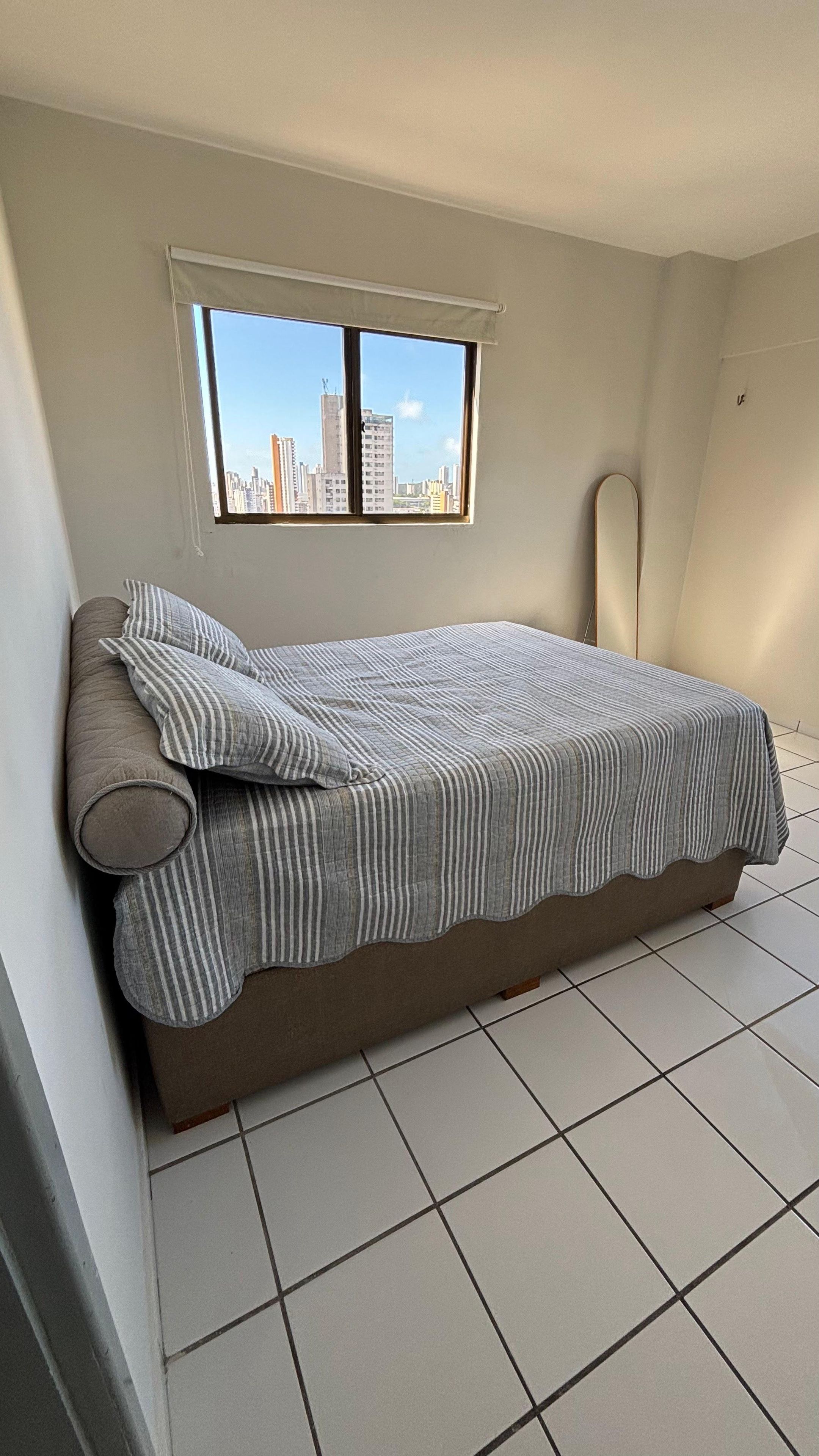 Quarto com cama, janela com vista para a cidade e piso de azulejos.