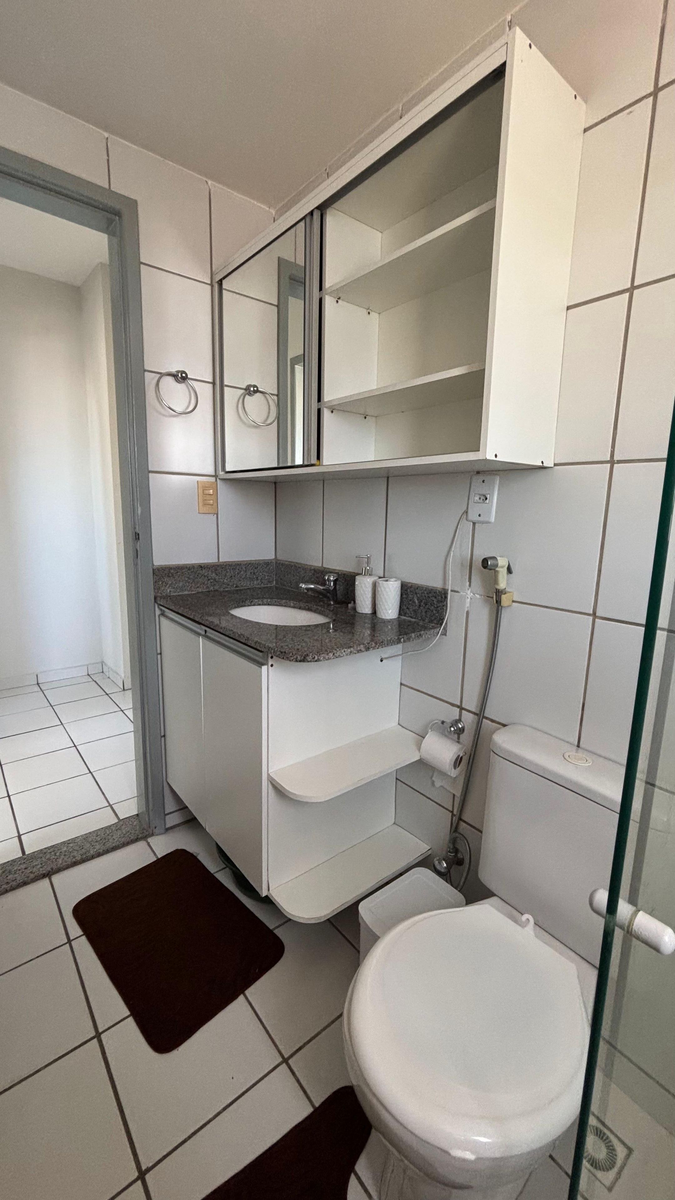 Casa de banho com sanita branca, lavatório com bancada de granito, espelho sobre o lavatório e zona de duche.