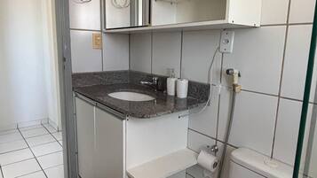 Casa de banho com sanita branca, lavatório com bancada de granito, espelho sobre o lavatório e zona de duche.
