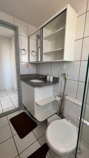 Casa de banho com sanita branca, lavatório com bancada de granito, espelho sobre o lavatório e zona de duche.