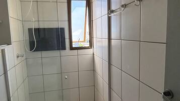 Casa de banho com chuveiro, sanita e janela que permite entrada de luz natural.