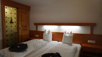 A hotel room with two beds, a wooden headboard, a nightstand, a bedside table, and a bathroom with a wooden door.