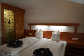 Ett hotellrum med två sängar, en sänggavel i trä, ett nattduksbord och ett litet bord vid sängen samt ett badrum med en dörr i trä.
