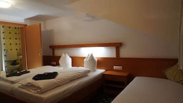 A hotel room with a single bed, a bedside table, a nightstand, and a bathroom visible through an open door.