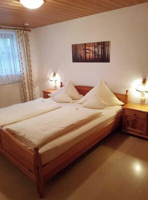 A bedroom with a wooden bed, white bedding, a painting on the wall, and bedside lamps. - Holiday Apartment With 1 Bedroom (Drachselsried)