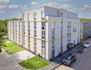A modern hotel building with a flat facade, multiple windows, and a parking area with cars. - Boutique Hotel Zuckerfabrik (Stuttgart)