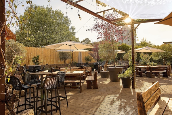 Un patio al aire libre con mesas, sillas, sombrillas y plantas en macetas.