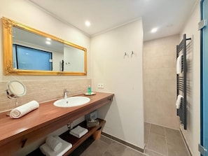 Un baño con tocador de madera, un espejo grande, un lavamanos y una zona de ducha.