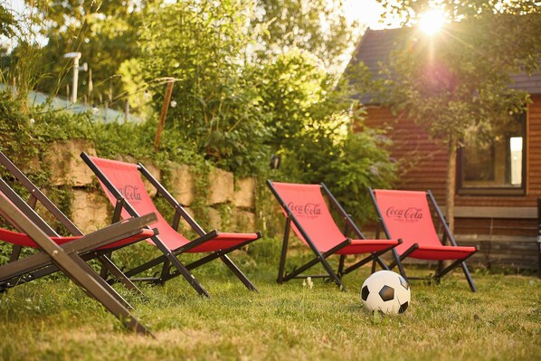 Des fauteuils de jardin avec le logo Coca-Cola, un ballon de football et, au fond, une cabane en bois.