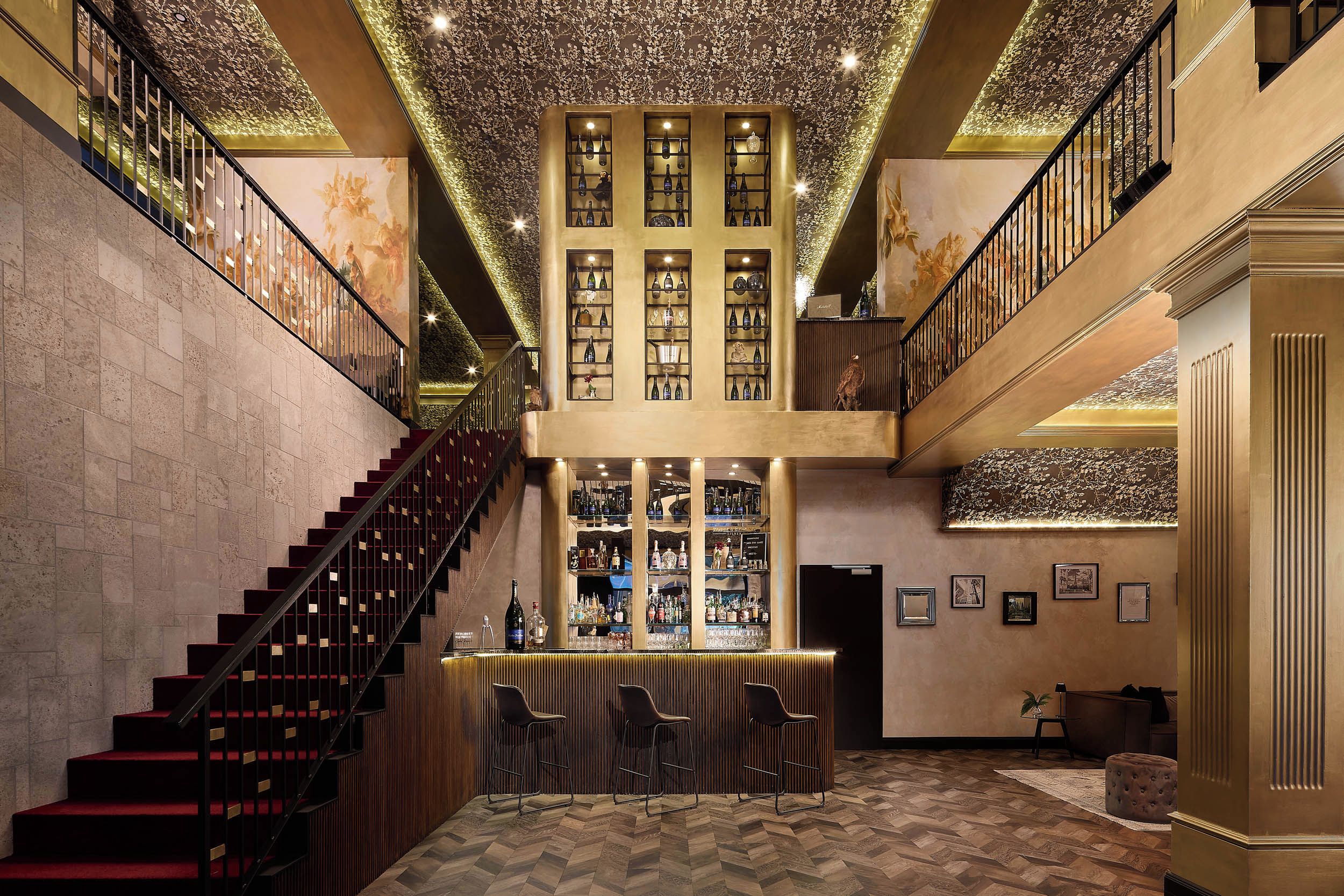 Eine prachtvolle Lobby mit einer zentralen Treppe, einer Bar und einer hohen Decke mit floralen Mustern.