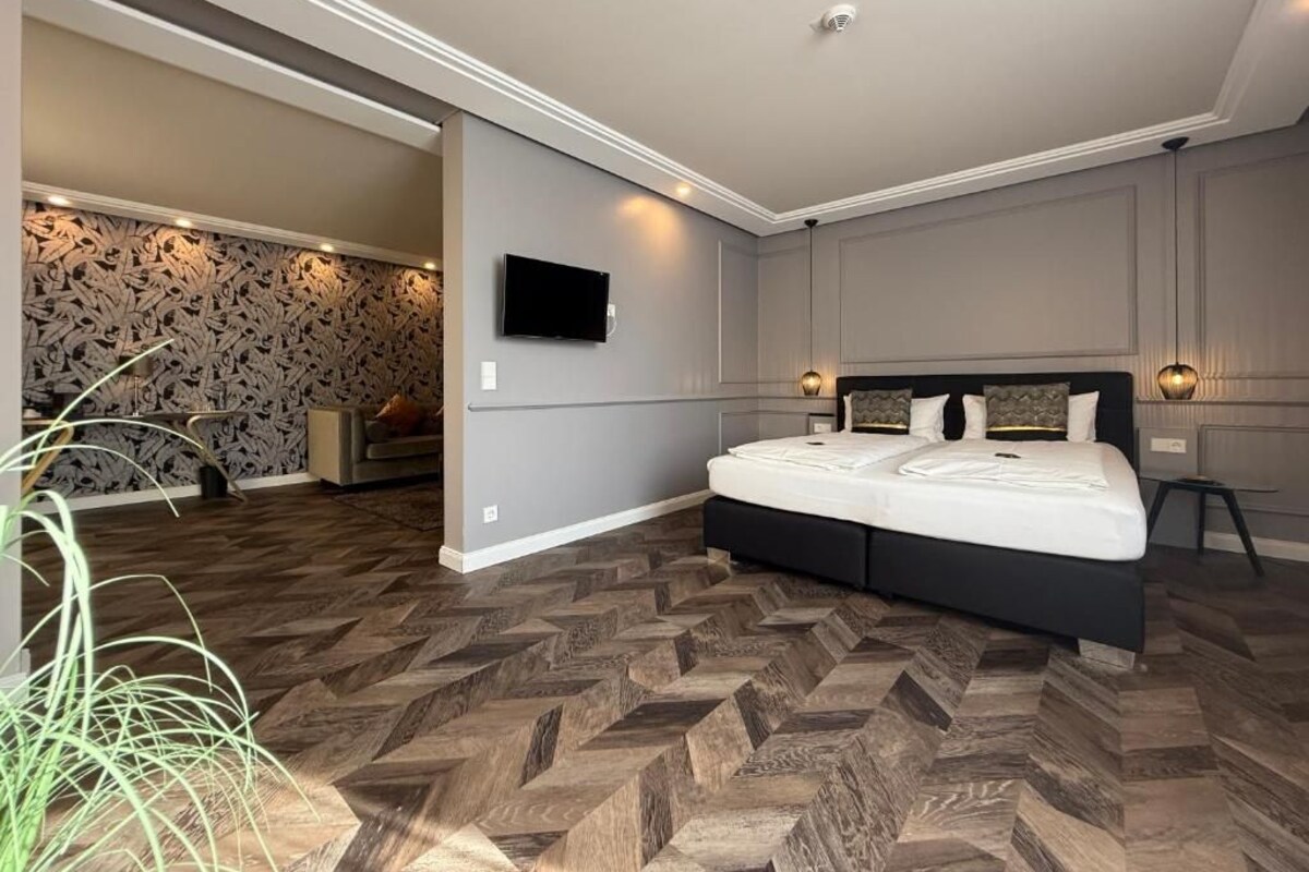 Une chambre moderne avec un grand lit, un téléviseur à écran plat fixé au mur et un parquet en bois disposé en motif chevrons.