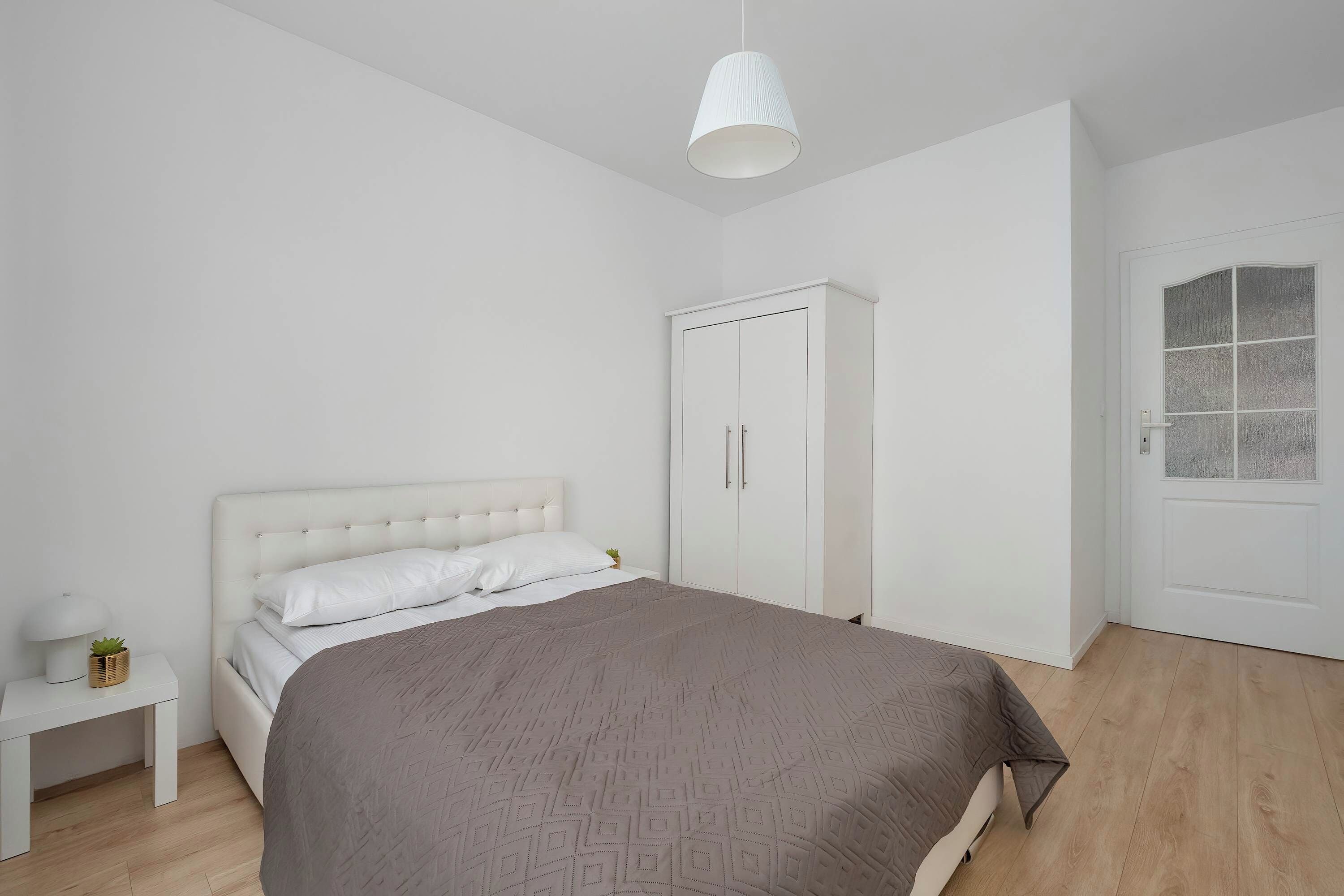 A bedroom with a bed, a wardrobe, a bedside table with a lamp, and a door with a frosted glass panel.