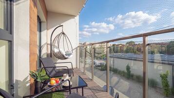 A balcony with a glass railing, a hanging chair, a table with a chair, and a potted plant.