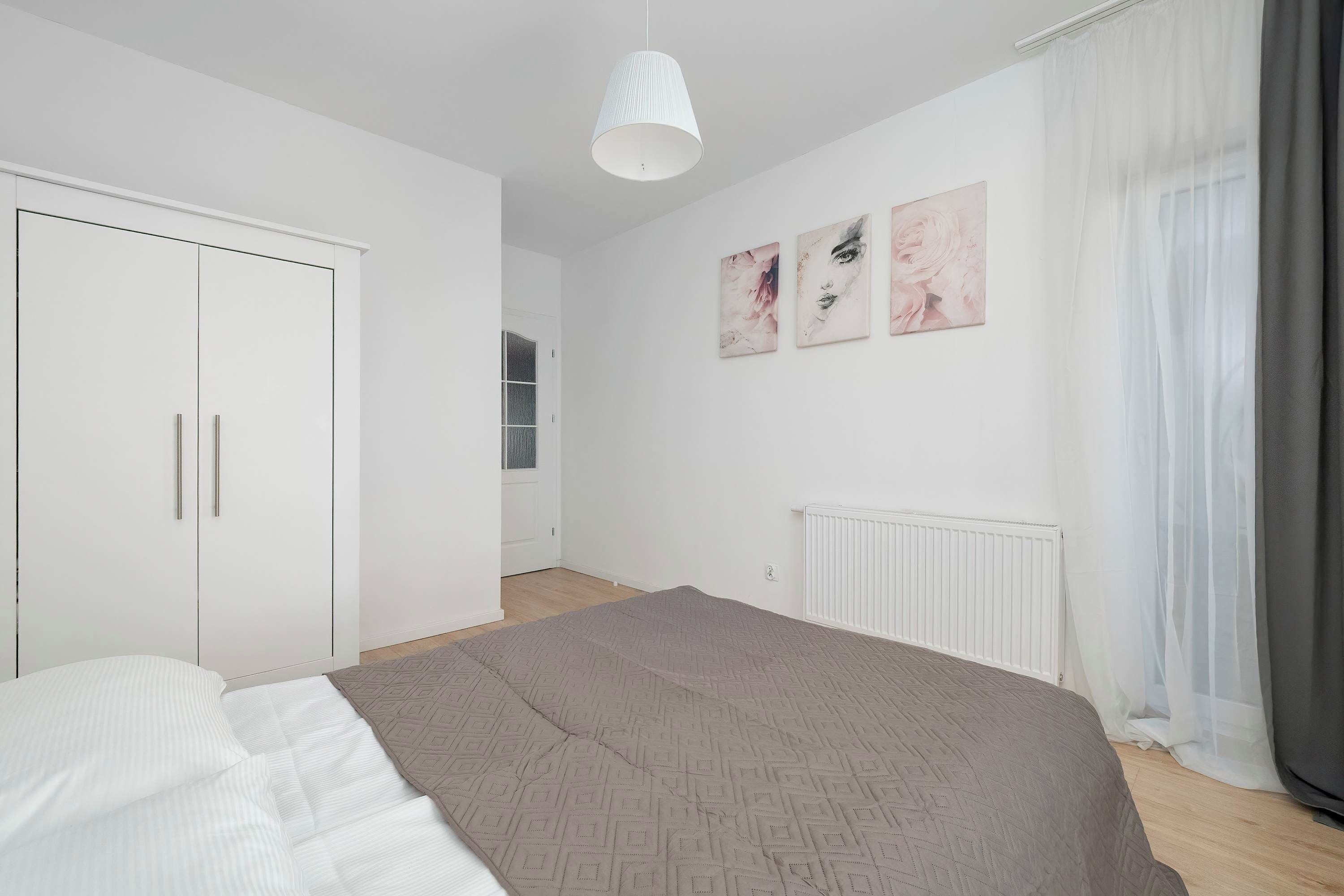 A bedroom with a bed, a wardrobe, a radiator, and a window with curtains.