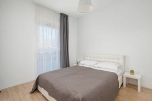 Quarto minimalista com uma cama grande, uma mesa de cabeceira e uma janela com cortinas.
