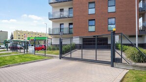 A gated parking area with a paved walkway leading to a modern building with balconies. - Łódź | Kazimierza Odnowiciela 13 | Family Apartment | Balcony (Łódź)