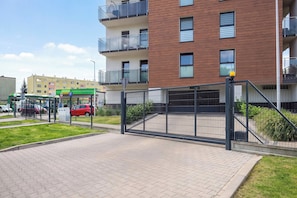 Área de estacionamento fechada com um caminho pavimentado que leva a um edifício moderno com varandas.