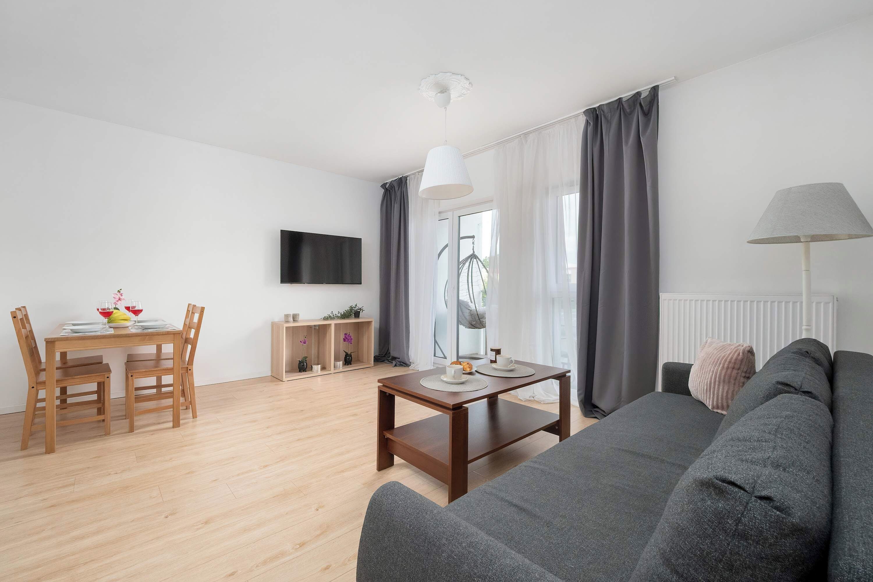 A modern living room with a grey sofa, wooden dining table, and chairs.