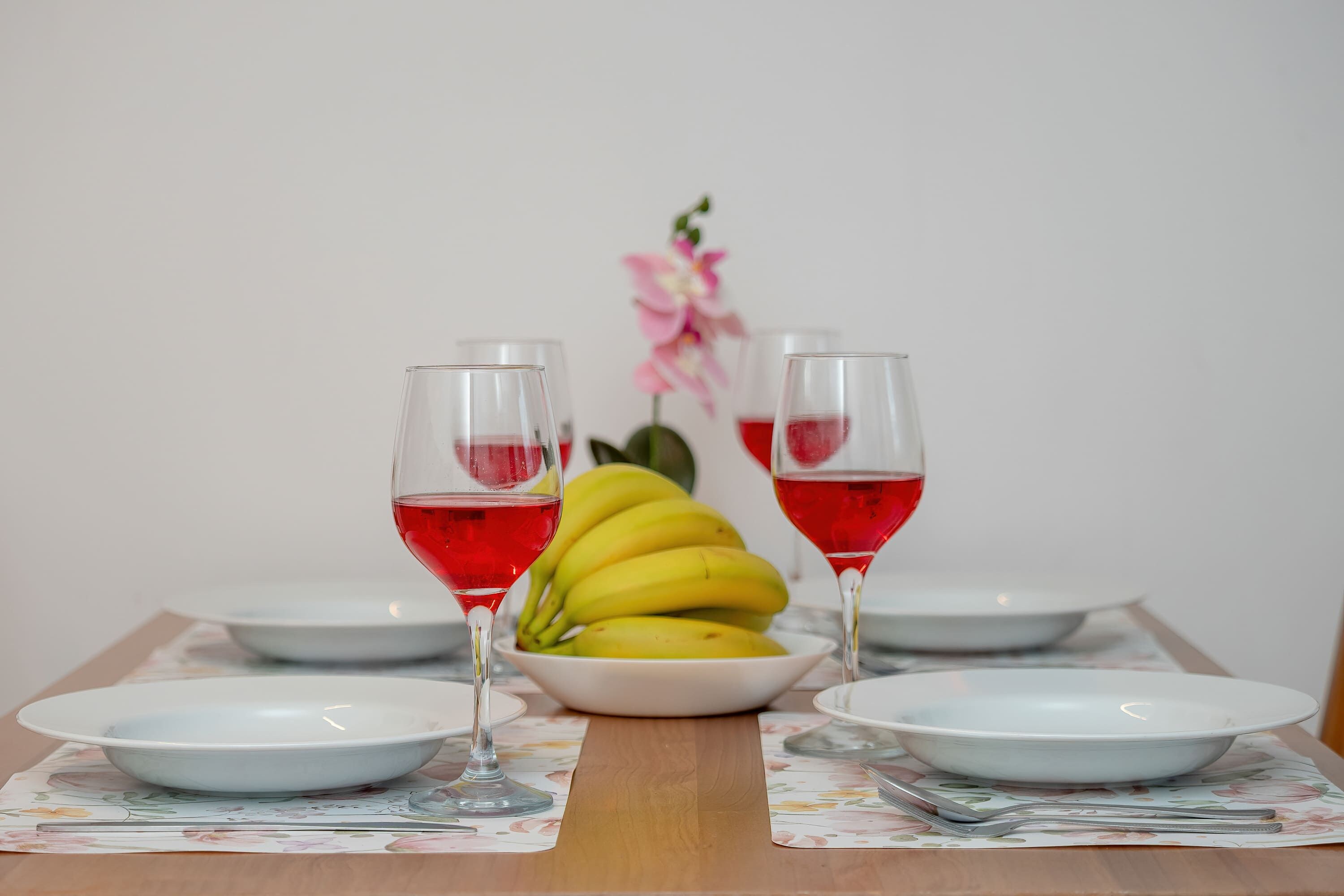 A table with a floral placemat, a bowl of bananas, and two glasses of red liquid.