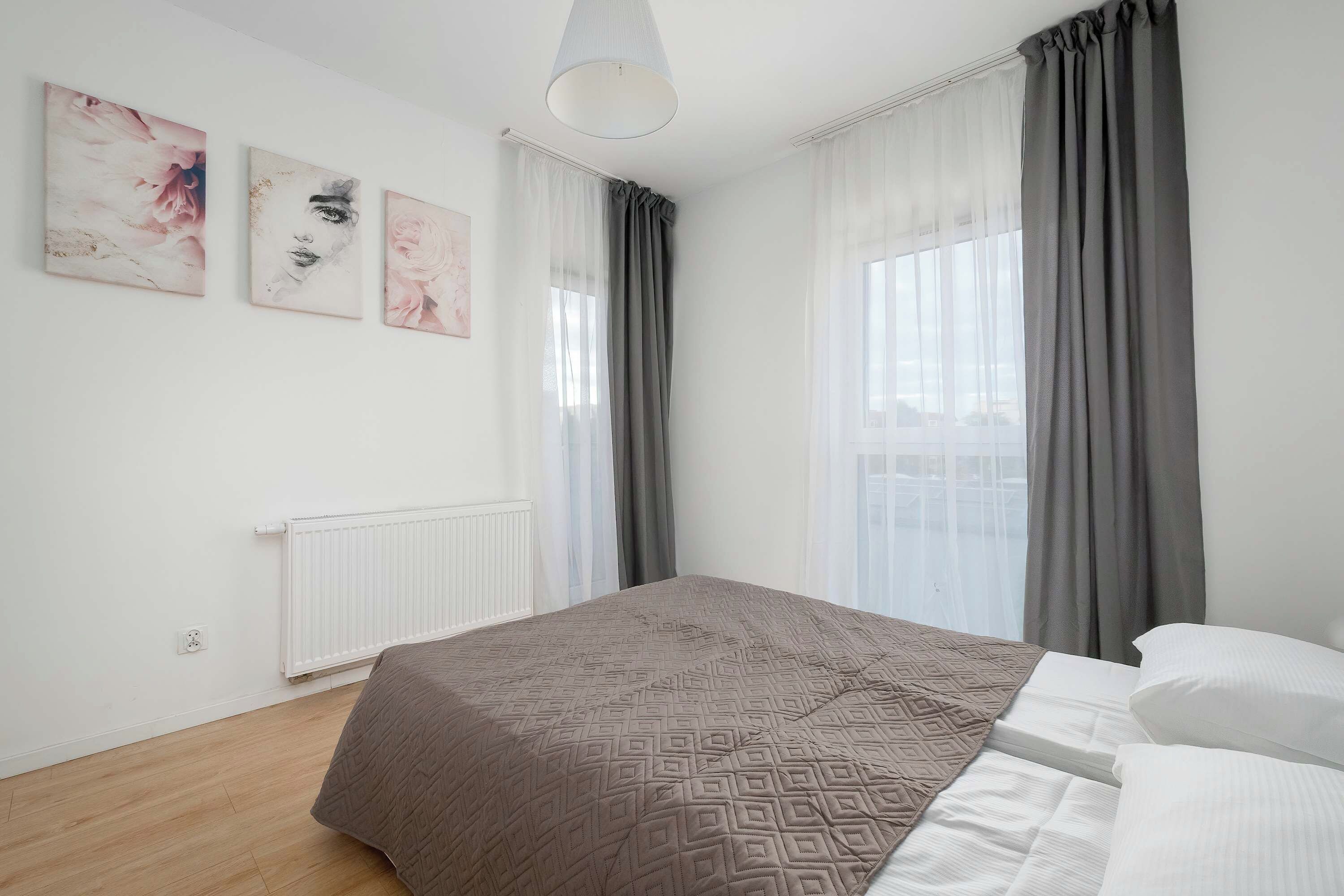 Een slaapkamer met een bed, een radiator en drie wanddecoraties.