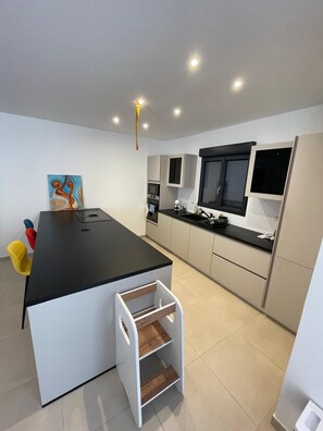 A modern kitchen with a central island, built-in appliances, and a small dining area with a chair. - HOUSE WITH A SWIMMING POOL, AIR CONDITIONING, AND A LARGE GARDEN (Vierzon)