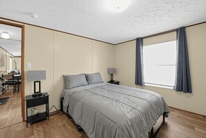 Et soveværelse med seng, sengeborde, lampe, vindue med gardiner og udsigt ud