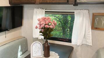 A compact RV interior with a dining table, a small TV, and a window with curtains.