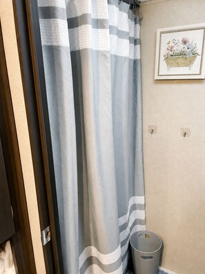 A bathroom with a striped shower curtain, a framed floral artwork on the wall, and a trash bin. - Cozy Country Escape with all the Amenities, Close to Taylor U, IWU, BSU (Upland)