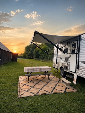 Un campamento montado con una caravana, una mesa de picnic y una manta sobre un campo cubierto de césped.