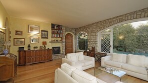 Sala de estar com lareira, sofás brancos, mesa de centro e parede de pedra.