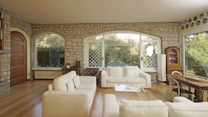 Una sala de estar amplia con paredes de piedra, ventanas arqueadas grandes y una chimenea.