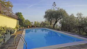 Piscina retangular com uma escada de metal de um lado, ladeada por um caminho de pedra e limitada por uma cerca de metal.